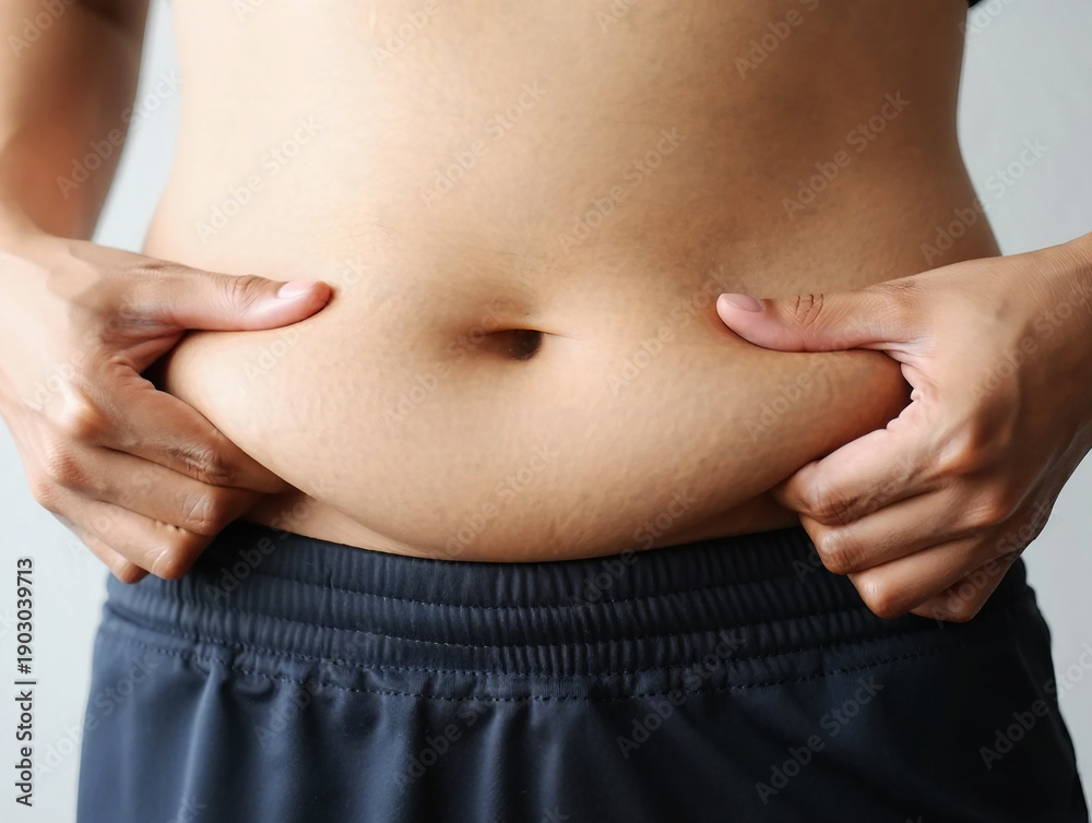 Naklejka premium Person pinching excess belly fat wearing dark athletic shorts skin