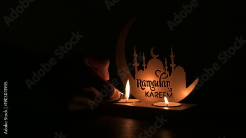 Hand lighting candles on Ramadan decor with mosque silhouette in dark ambience