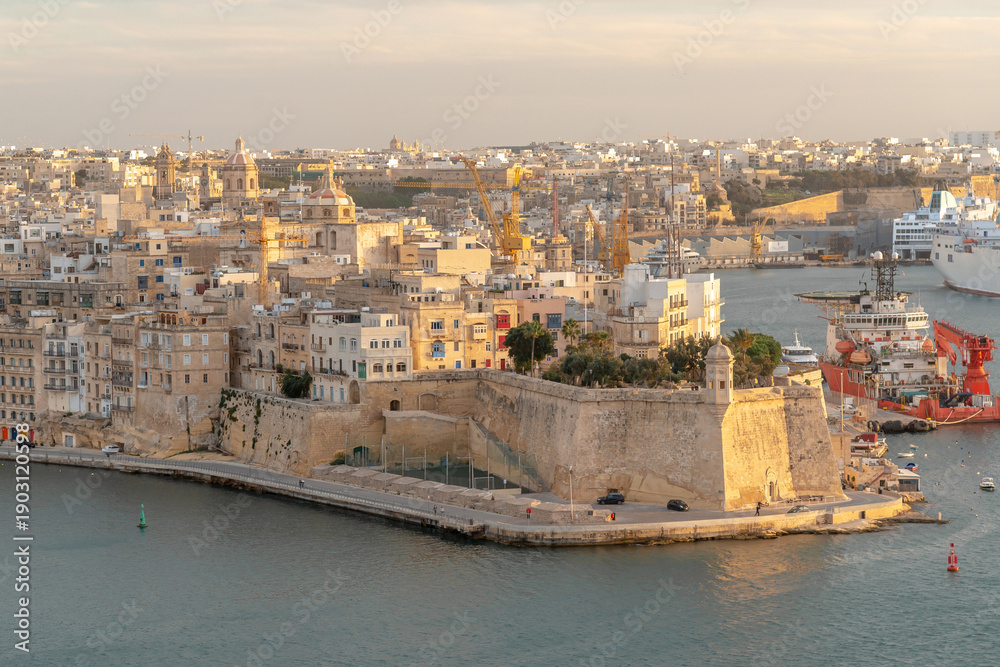 Fototapeta premium Stunning aerial view of Senglea's fortifications and Gardjola Gardens in Malta at sunset. Perfect for Mediterranean travel, maritime industry, and heritage tourism marketing.
