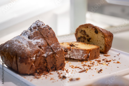 Sliced homemade fruit cake with raisins and powdered sugar on a white tray. Close-up of delicious traditional loaf cake on a bright background