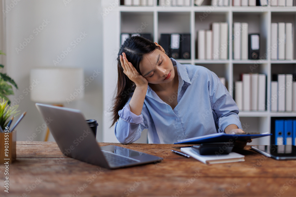 Fototapeta premium Businesswoman work financial documents is feeling stressed and having a headache while working late at her desk in the office, 