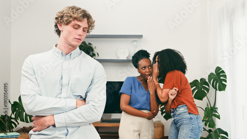 Bild auf Leinwand Bullying in Workplace - Two Women Whispering While Man Stands Apart With Arms Fo