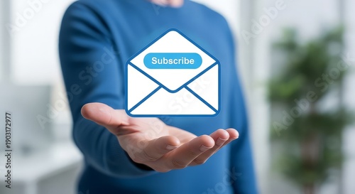 Person holding subscribe email icon in hand blue shirt office background newsletter concept