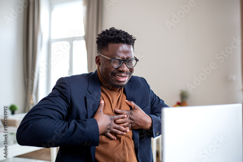Fotografie African American businessman experiencing sudden chest pain or heart attack while working at a laptop