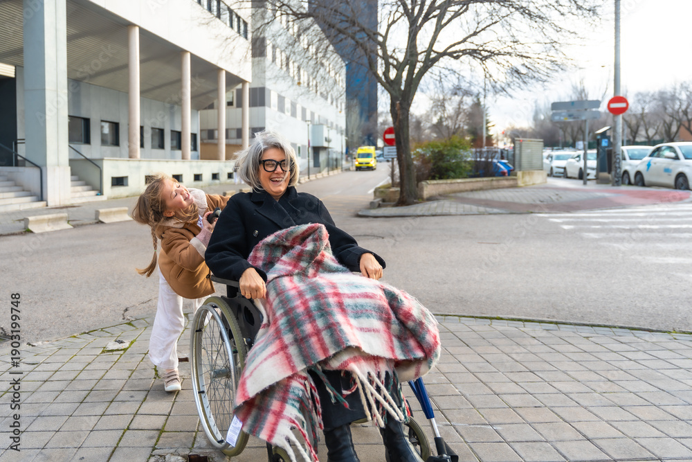 Obraz premium Granddaughter pushing smiling grandmother in wheelchair outdoors