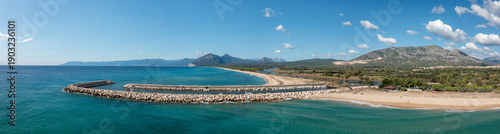 Foto Panoramic aerial view of a curved stone breakwater enclosing turquoise waters, sandy beach, and green countryside with rugged mountains under a clear blue sky near Orosei, Sardinia