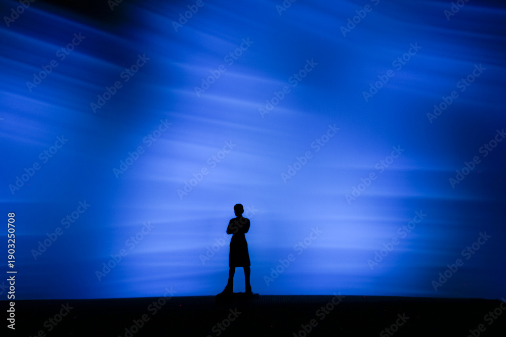 Fototapeta premium Silhouette of a person standing alone against a powerful blue light