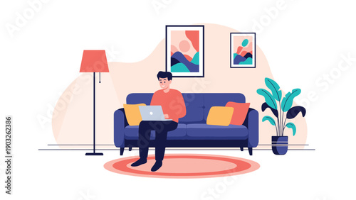 Young man sits comfortably on a blue sofa in his living room while working or browsing on a laptop during his leisure time at home.