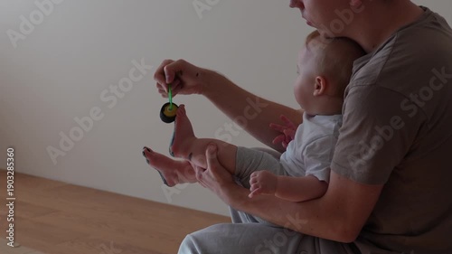 Close up video of a dad applying black paint to a baby foot using a roller. Preparation step for diy footprint art indoors 
