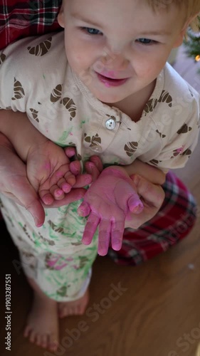 mother hugging a toddler while sitting near a decorated christmas tree indoors. adult holding the child from behind. holiday home setting with soft natural light.
