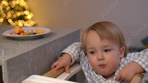 toddler taking a piece of fruit from a plate on the table and eating it.
