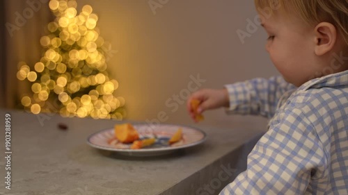 toddler taking a piece of fruit from a plate on the table and eating it.