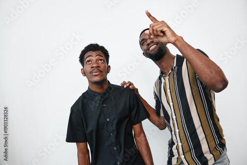 Cuadro en lienzo Two African American men with dark skin standing together on white background, one pointing up and the other looking in the same direction with casual clothing and friendly expressions