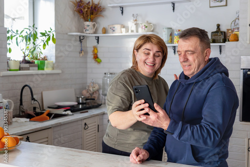 Принти на полотні mature couple stands together in the kitchen making a video call with family while preparing a meal at home