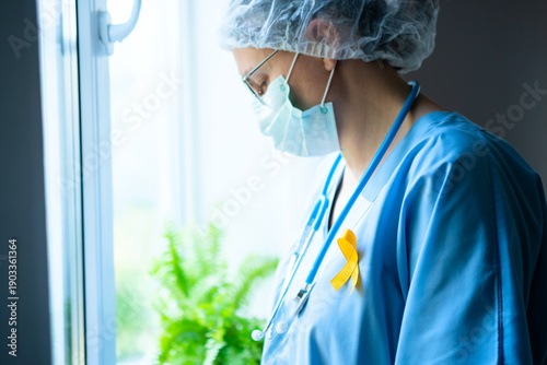 A female medical professional wears a yellow satin ribbon on her uniform, symbolizing awareness for suicide prevention, sarcoma, and childhood cancer.
