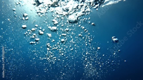 Underwater bubbles rising to the surface in clear blue water with sunlight.