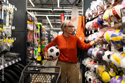 Woman shopping for sports equipment and holding a soccer ball in a sporting goods store during the day