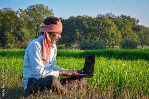 Indian rural man using laptop at agriculture field. Modern technology in agriculture