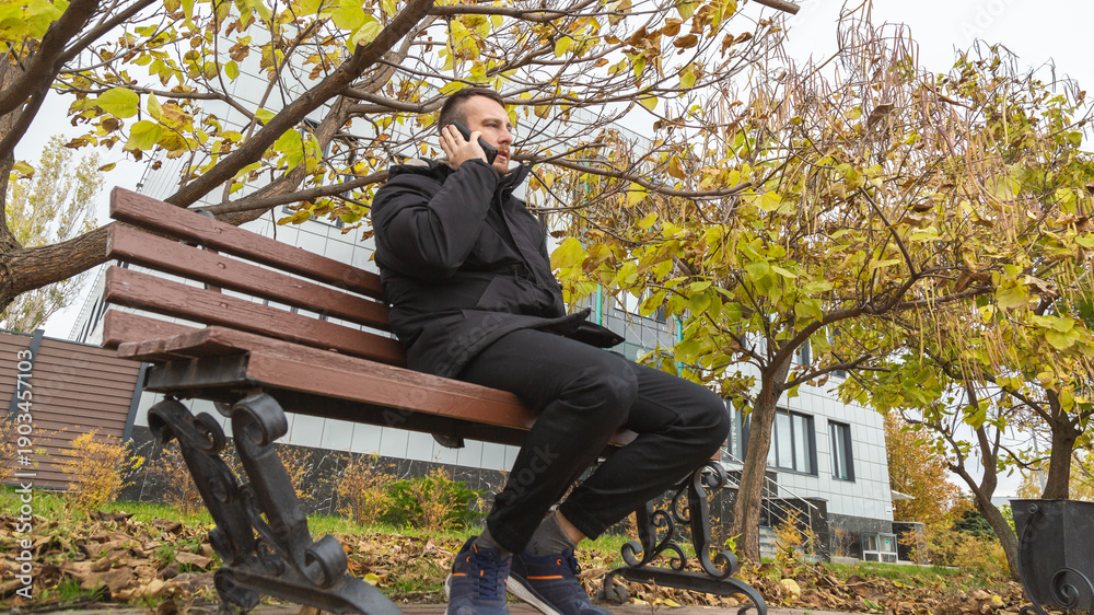 Fototapeta premium young man is looking at his phone, man in casual casual wear enjoying the autumn weather in street