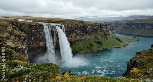 Waterfall cascading over a cliff into a vast, turquoise lake under a cloudy sky