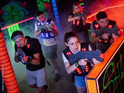 Friends having fun playing laser tag in colorful neon arena with red and green lights. Teamwork and entertainment at leisure center.
