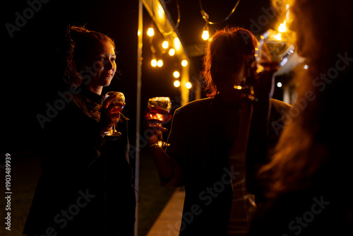 Obraz na płótnie Group of friends enjoying a nighttime gathering with drinks under warm decorativ