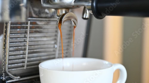 Close-up of espresso extraction from a professional coffee machine into a white cup. Hot coffee flowing from portafilter. Concept of coffee making, barista work, cafe routine, brewing process.