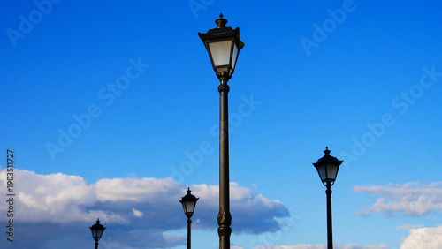 Fotografi Black beautiful street lampposts against the blue sky