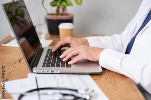Quadro su tela Medical Professional Typing on Laptop at Desk With Documents, Stethoscope, Coffe