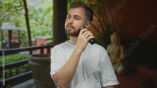 Foto Man shaves beard with electric razor while holding the razor to his jaw in a hotel building; grooming confidence