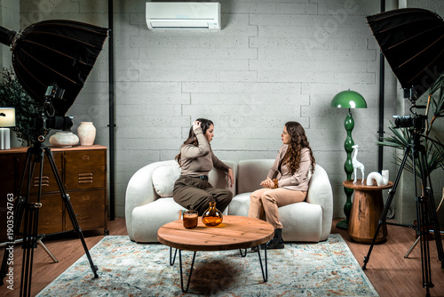 Photography Two women sitting on a sofa, conversing during a podcast or interview recording