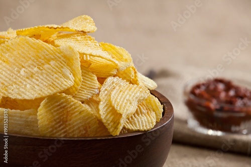 Crispy ridged potato chips in a wooden bowl with tomato salsa dip on a rustic wooden background