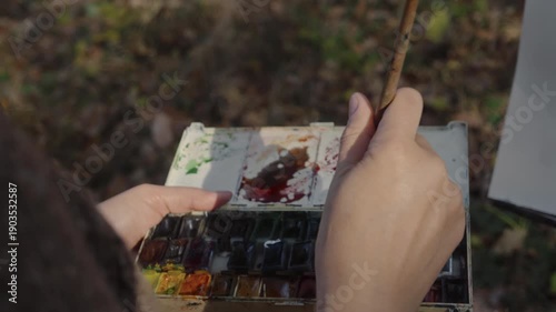 Close-up, the artist breeds a palette of watercolor paint to paint a landscape of an autumn forest