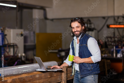 Professional industrial engineer in blue hard hat using a digital caliper and laptop for quality control in a metal factory. Precision manufacturing and small business concept.