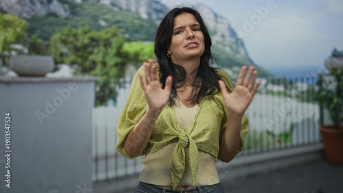 Photos Young hispanic woman holds hands up in building entrance with tense posture and turned palms; denial