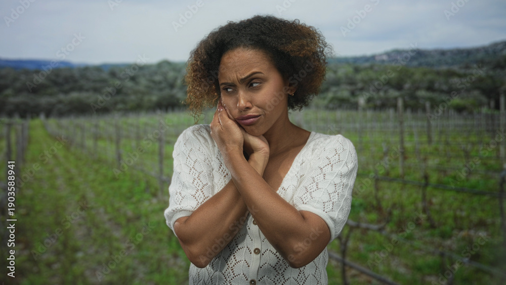 Fototapeta premium Woman with hand on cheek in a vineyard field, crossing arms and wincing in pain for toothache; distress toothache worry.