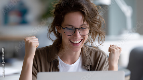 Excited woman celebrating success, fists pumped in the air, looking at laptop screen with joy