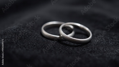 Minimalist composition of two silver wedding rings on dark velvet with subtle glow. lifestyle magazines, social media lookbooks, designed for lifestyle magazines and social media content.