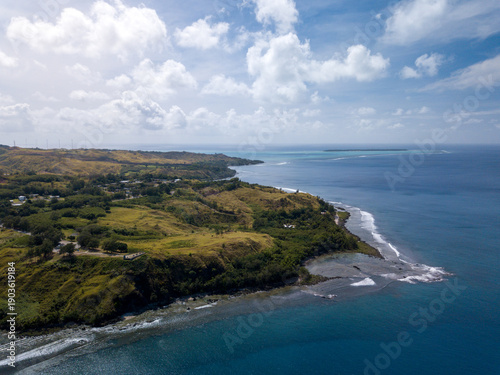 Aerial view of the coastline where the lush green vegetation meets the turquoise sea under the scattered clouds, Guam, United States.