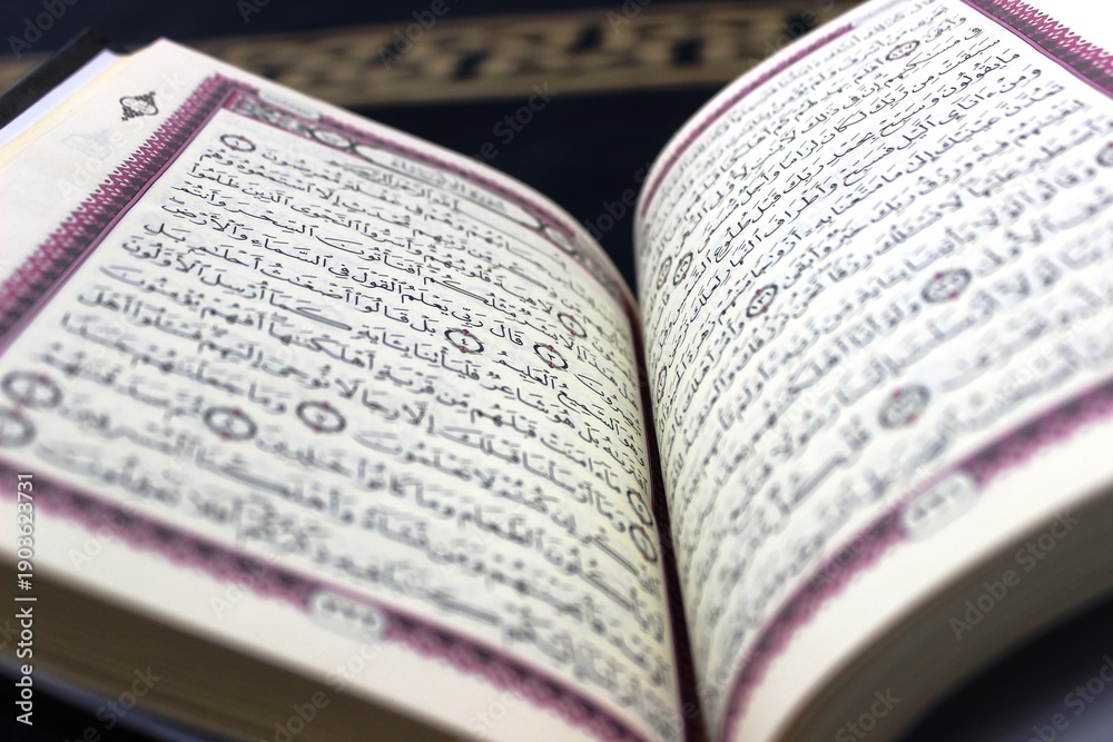 Fototapeta premium Holy Quran open on a prayer rug in a mosque - Islamic concept A high-quality close-up of the Holy Quran pages, placed on a traditional blue prayer rug inside a mosque. 