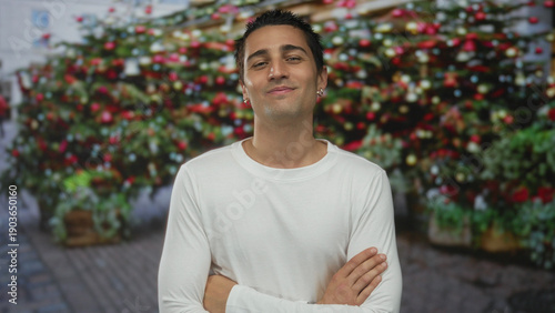Slika na platnu Young hispanic man in a white shirt with arms crossed outside a rustic flower shop on cobblestone street; rejection
