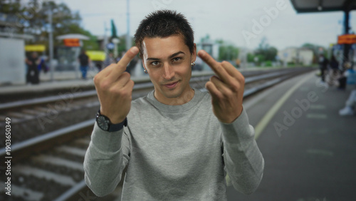 Obraz na plátně Young hispanic man flips both middle fingers directly at camera in a busy train station; anger defiance