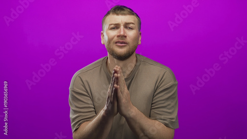 Vászonkép Man young overweight pressing palms together in a prayer pose in a purple studio setting with visible beard and folded hands; pleading remorse vulnerability