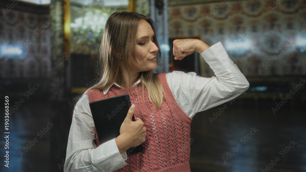 © Krakenimages.com - Woman indoors at museum holding book and flexing in sweater showcasing confidence and education in historical setting with soft lighting.
