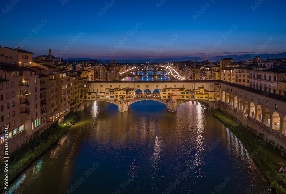 Obraz premium Iconic Ponte Vecchio bridge illuminated at blue hour with reflections on the Arno River in Florence, Italy. Historic architecture and evening city lights create a classic European cityscape