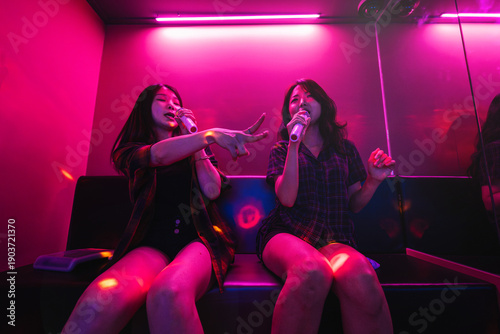 Photography Asian female friends singing K-pop song in a noraebang karaoke, having fun toget