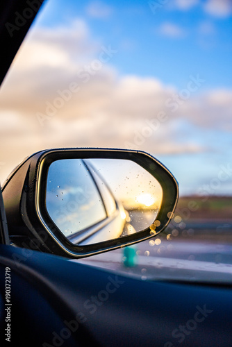 A car's rear view mirror reflects the sun