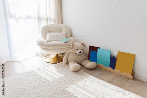 Fotografija Bright minimalist nursery corner with cozy armchair, teddy bear and colorful children books in natural light