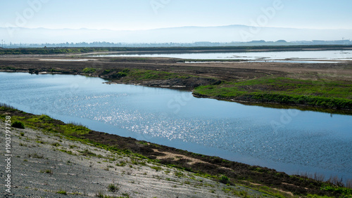 Tableau sur toile Sunlit waterway reflecting bright light between green banks and stone‑lined edge