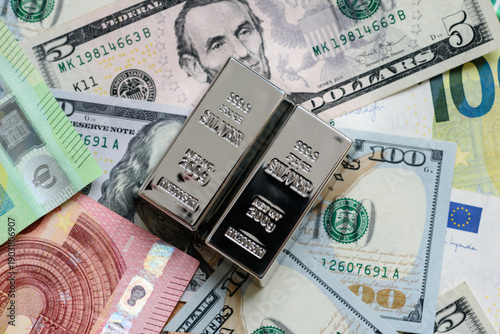 A silver bar, white metal against a backdrop of money, as a concept for the sales. A silver bar